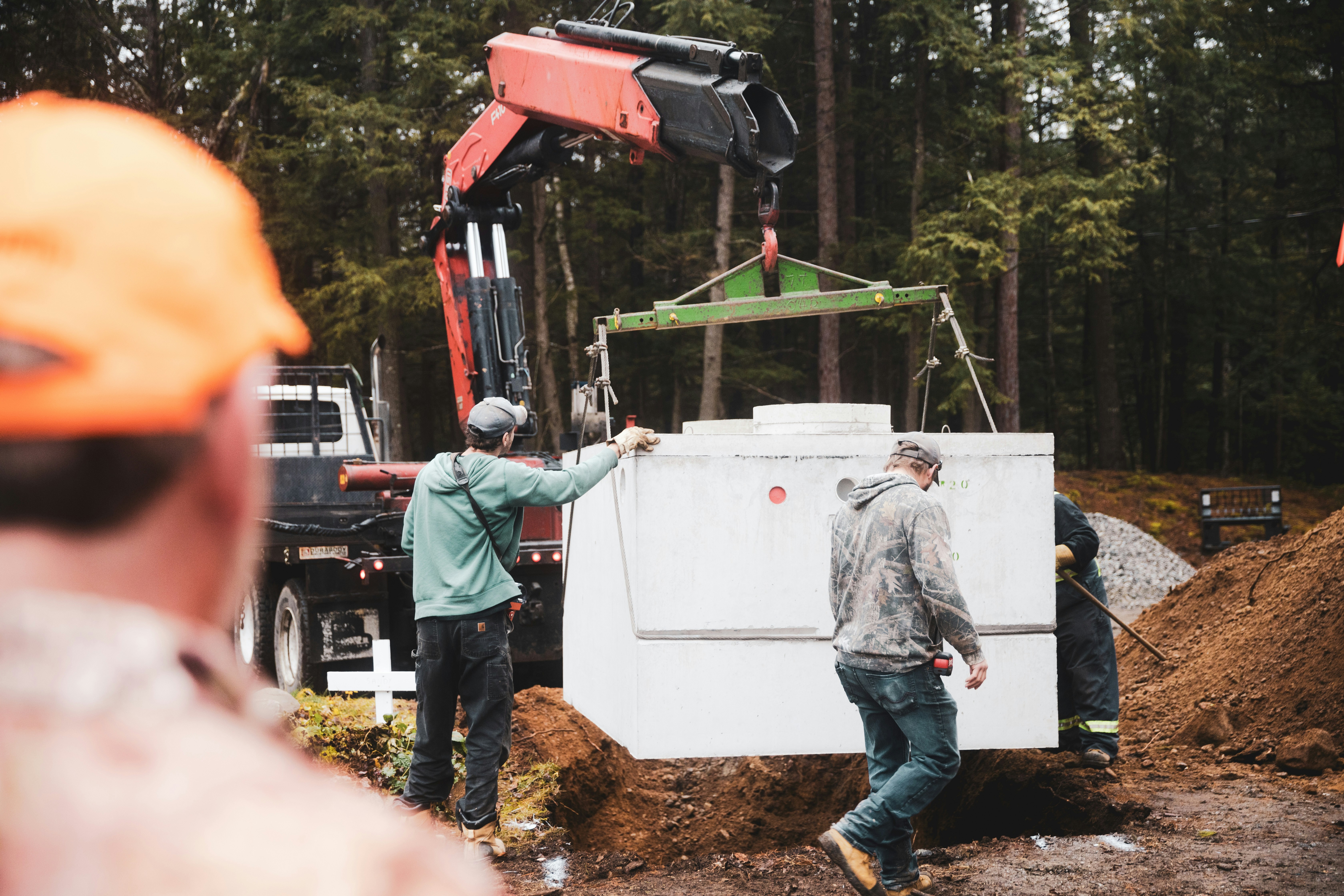 A septic crew lowering a new concrete septic tank into place on a rural job site